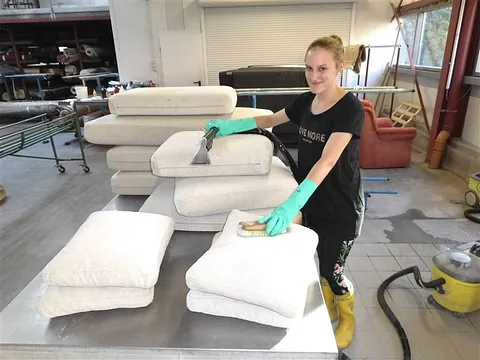 Person reinigt weiße Teppiche mit Bürste und Reinigungsgerät in einer Werkstatt für Teppichreinigung